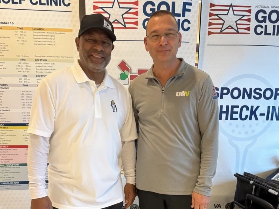 Chapter 12 member Andre Anderson and National DAV Commander John Donovan smiling together in front of National Disabled Veterans Golf Clinic banners.