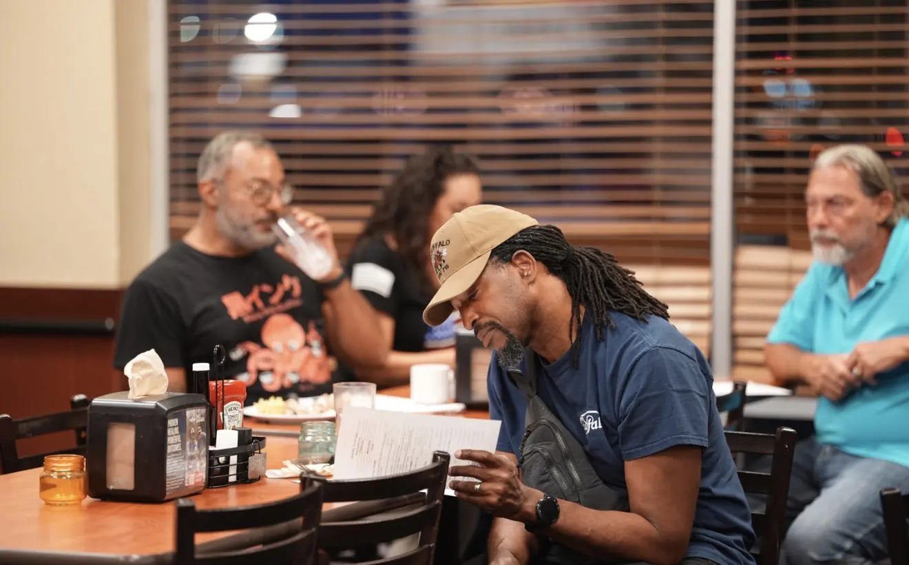 Members follow the agenda at their table while one takes a drink.