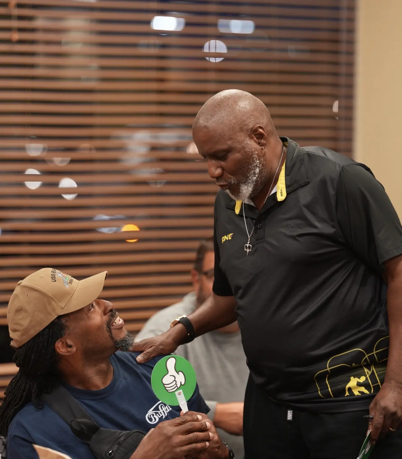 A member leans in to greet a seated Veteran holding a green voting paddle.