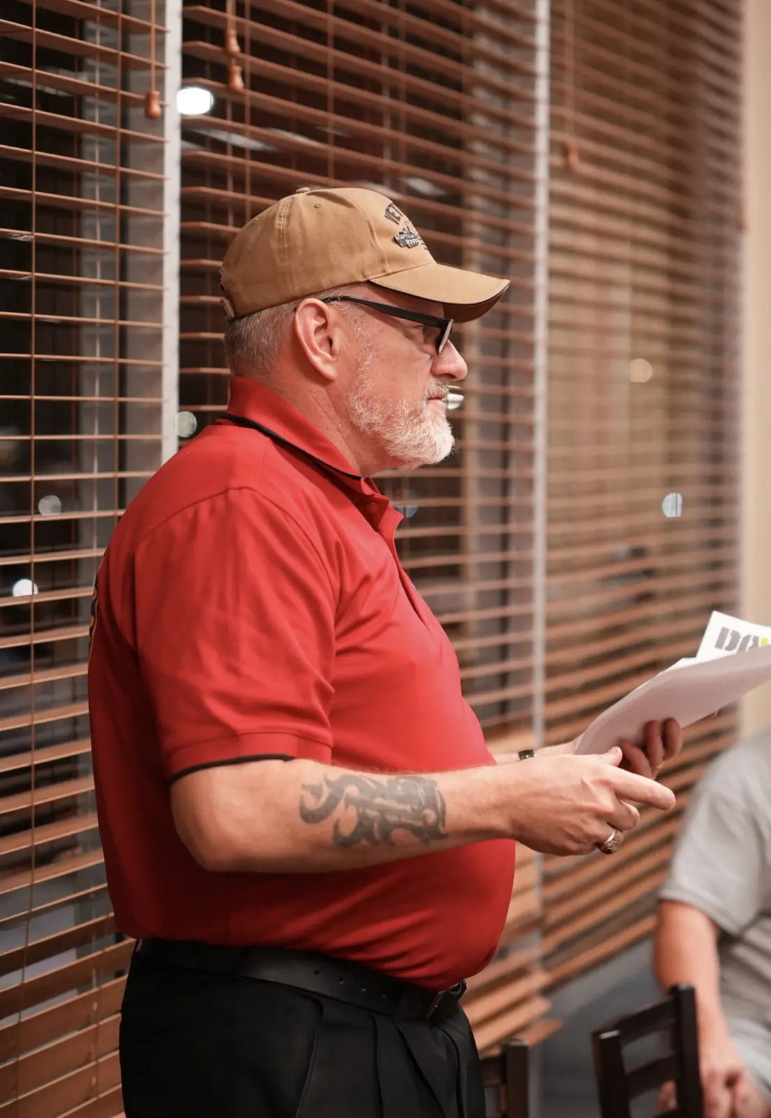 A member in a red polo reads from his notes at the front of the room.