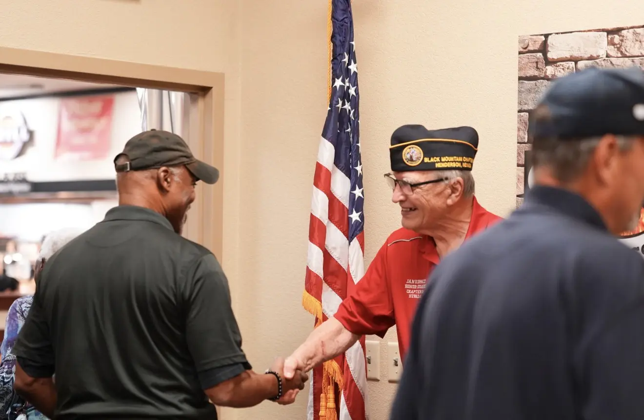 Two members shake hands in front of the American flag.