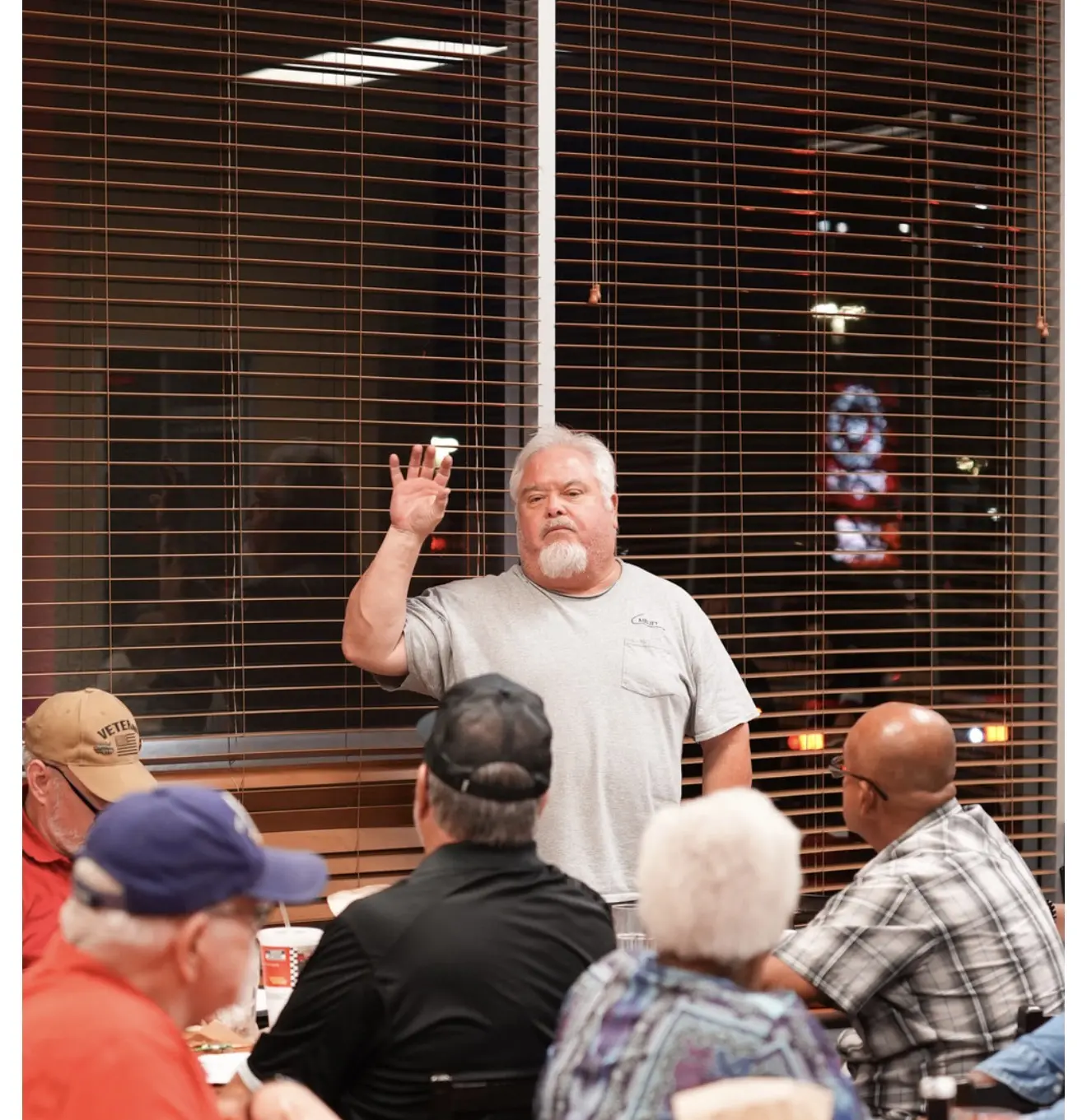 A member raises his hand to speak while the room listens.