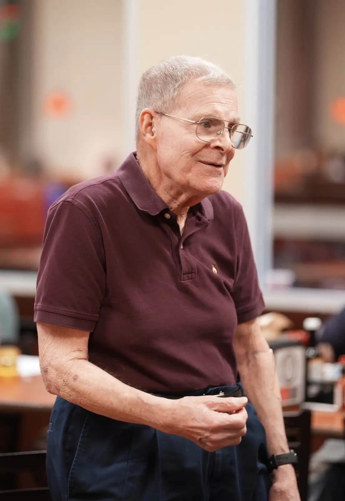 An older Veteran in a maroon polo smiles as he greets fellow members.