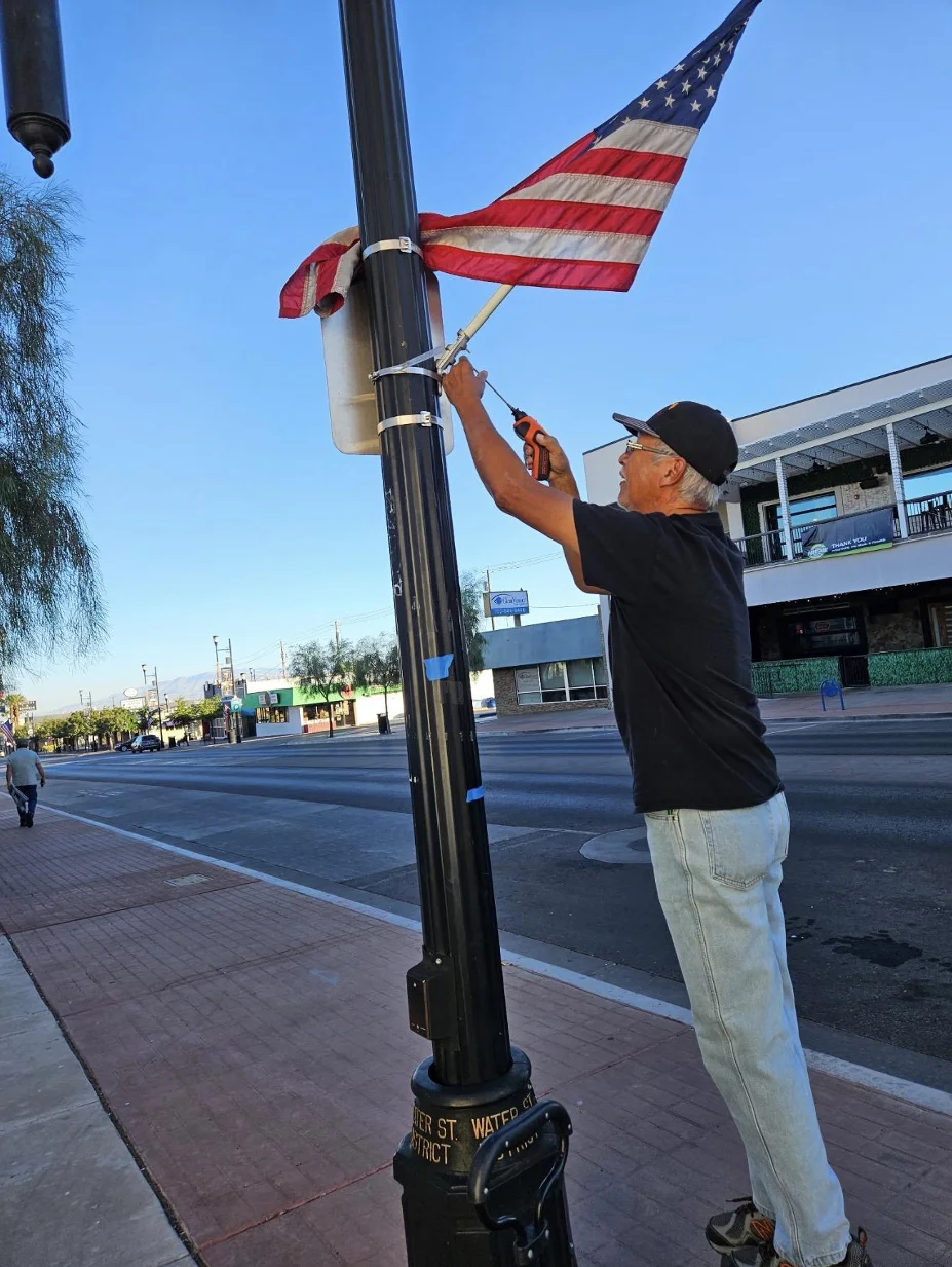 A Veteran works at the ties holding a flag bracket to a Water Street light pole.