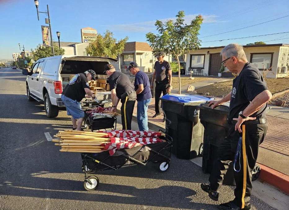 Honor Guard members collect flags on their wooden poles into a wagon beside a white pickup truck.