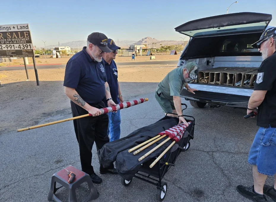 Members roll a flag around its pole and lay the flags in a wagon behind an open pickup truck.