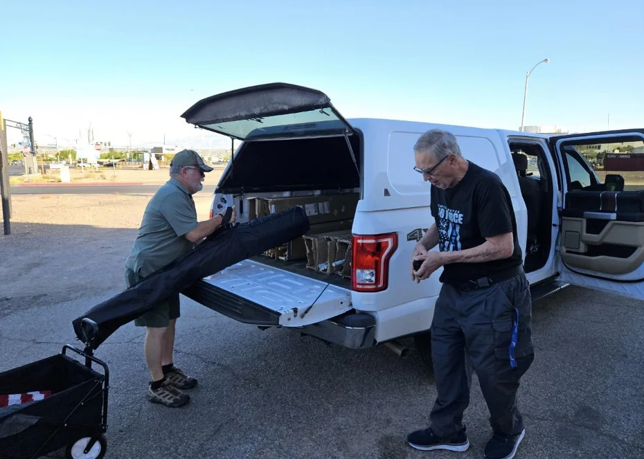 Two members load a flag carry bag into the back of a white pickup truck as the morning wraps up.